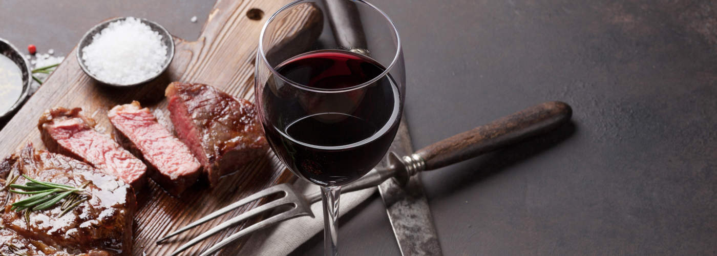 Red Glass of Wine with Cooked Sliced Steak on Cutting Board with Herbs and Spices